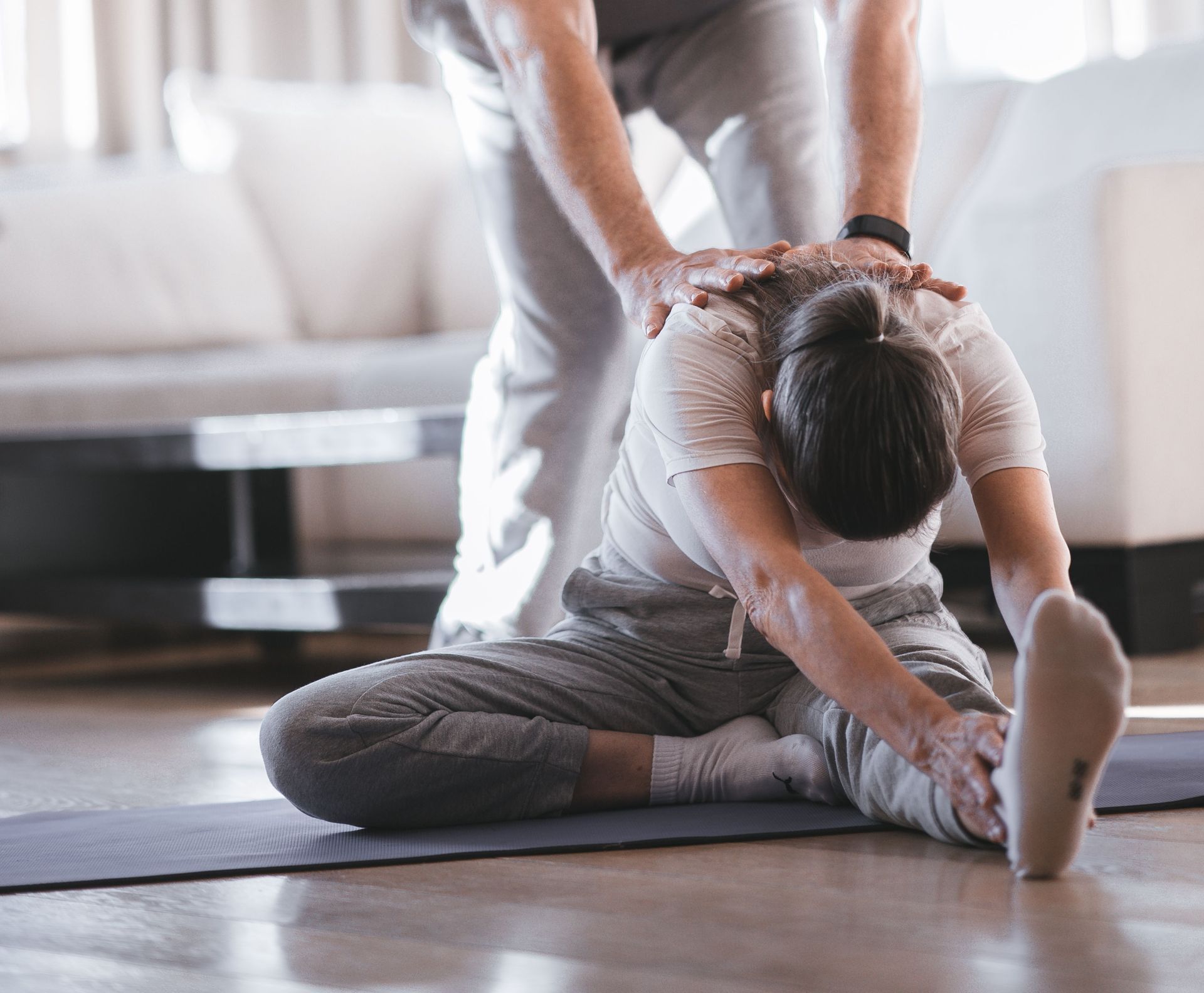 Senior man helps with partner stretch in bright indoor setting, promoting flexibility.