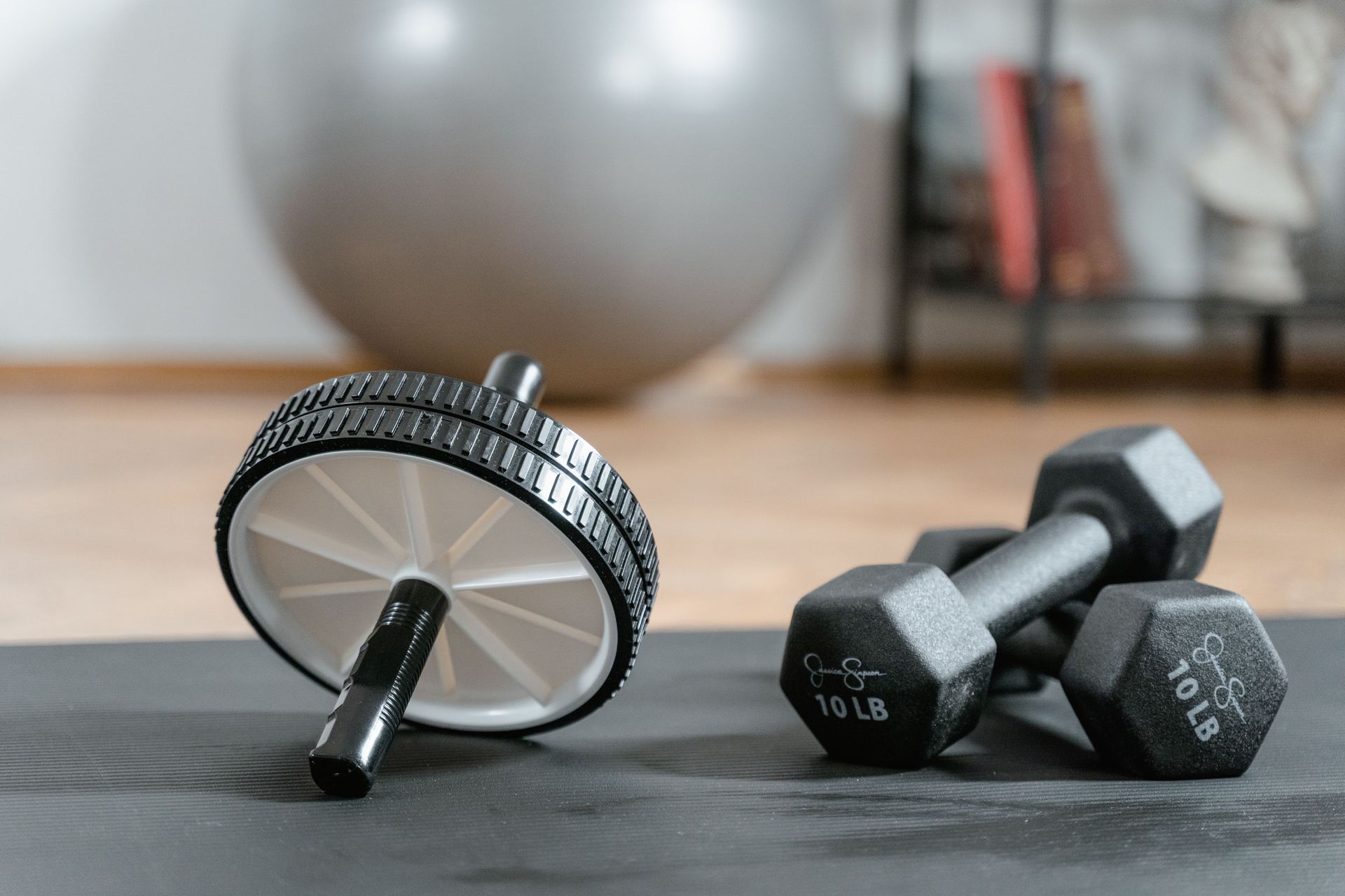 Close-up of ab wheel and dumbbells on a mat in a home gym setting.