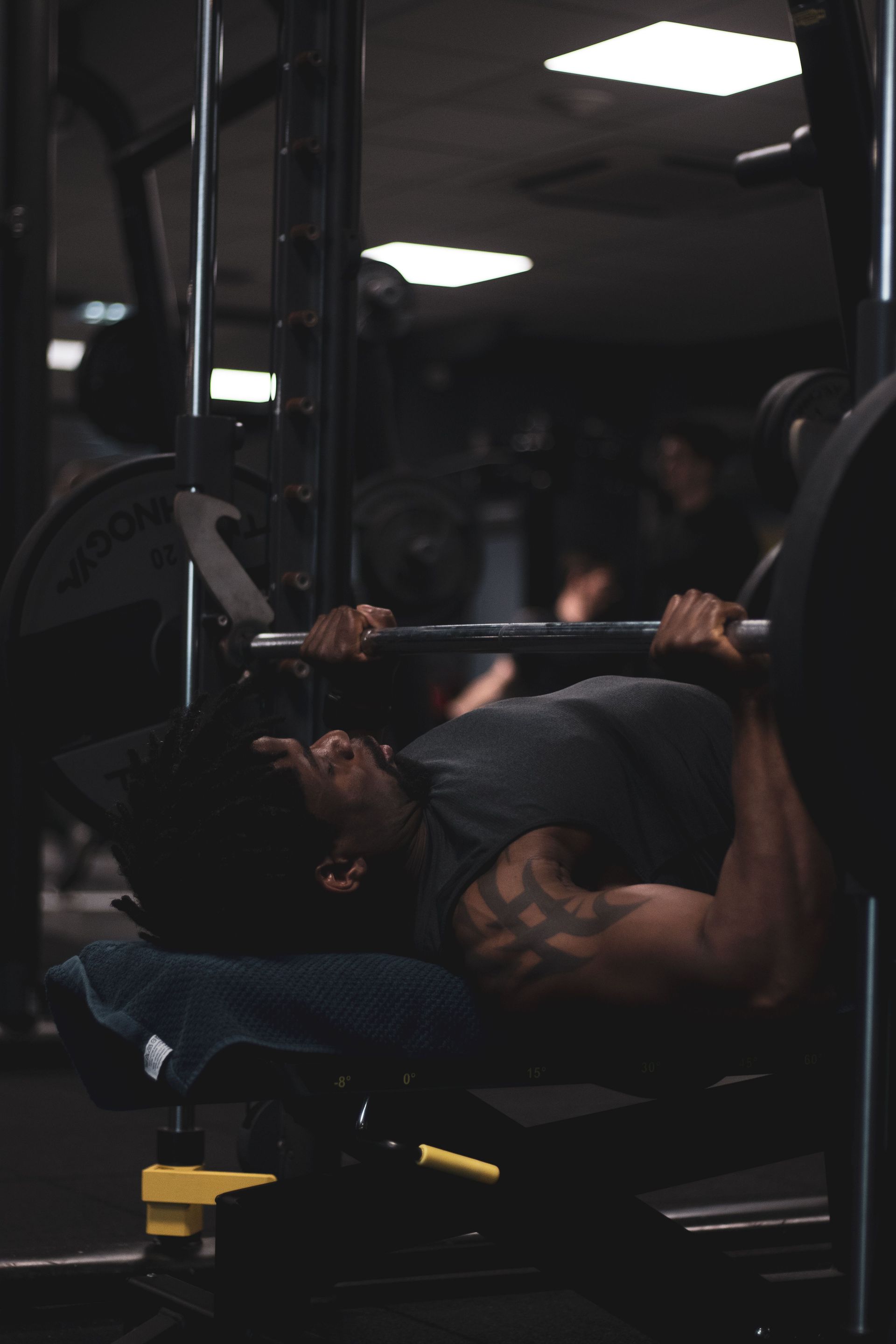 Man performing bench press in a dimly lit gym, focused on weight training.